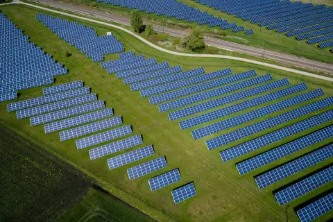 Aerial view of a solar farm: rows of panels across a grass field beside a railway