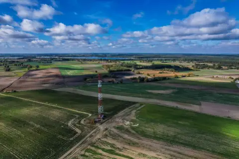 A radio mast standing in open farmland under a blue sky with white clouds