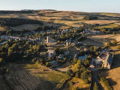 Aerial view of Abbotsbury in Dorset at golden hour: a stone village with its church and abbey barn among fields, under rolling downs